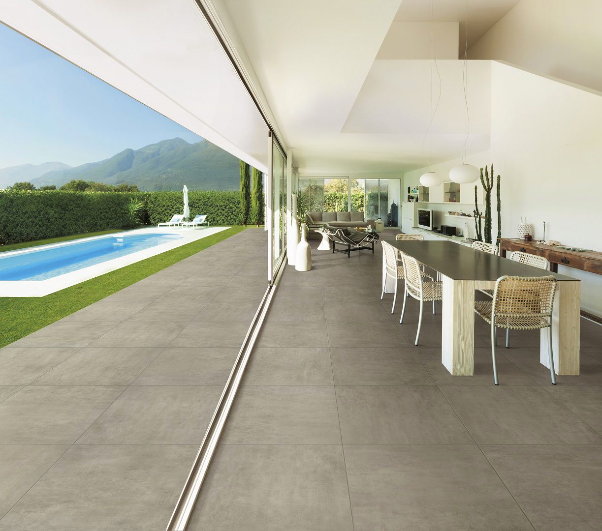 Patio moderne avec longue table à manger, chaises en osier, vue dégagée sur la piscine, la pelouse et les montagnes