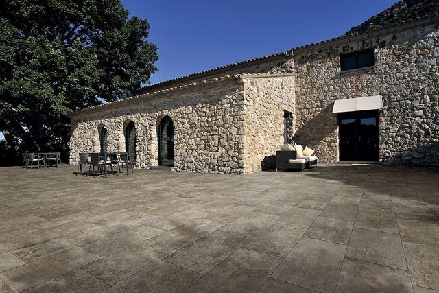 Cour en pierre jouxtant un bâtiment rustique en pierre avec des fenêtres cintrées.