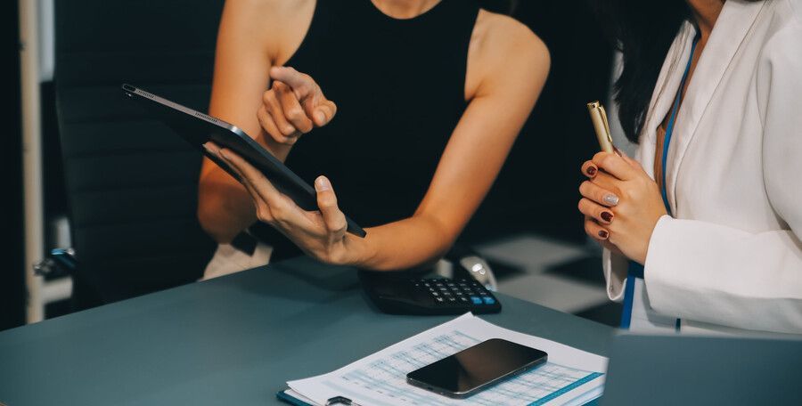 Dos personas sentadas a una mesa revisando una tableta y documentos, con un teléfono y un bolígrafo cerca.