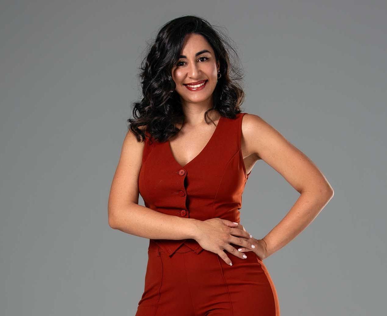 Una mujer con un mono rojo está de pie con las manos en las caderas y sonriendo.