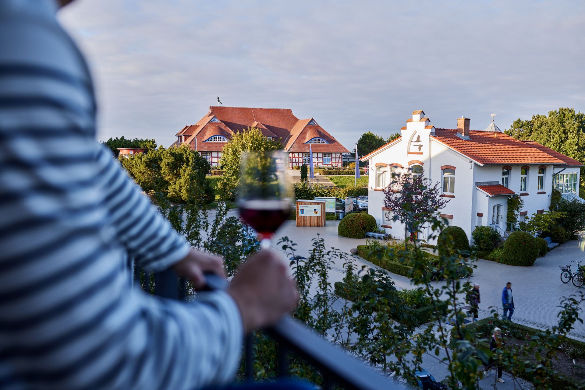 Person auf dem Balkon hält ein Weinglas und blickt auf das Zentrum von Zingst.