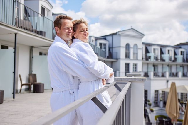 Ein Paar in weißen Bademänteln auf einem Balkon, die in den Hotelgarten blicken.