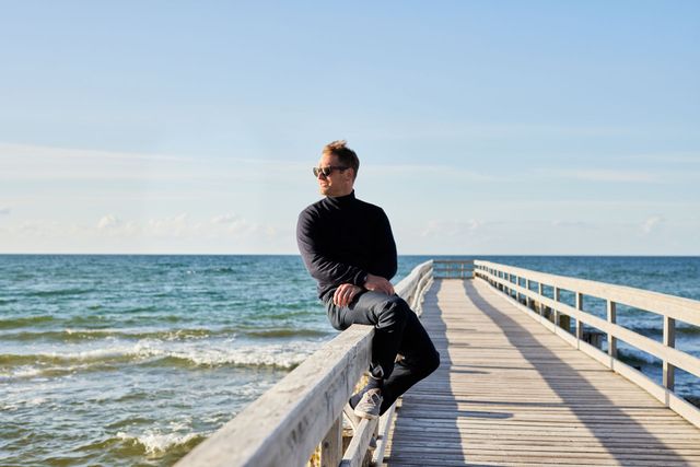 Ein Mann sitzt auf dem Geländer eines Fischerstegs und blickt auf die Ostsee.