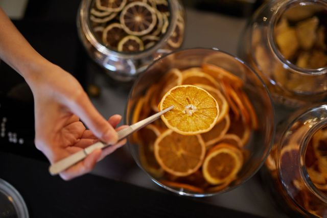 Mit einer Pinzette eine getrocknete Orangenscheibe aus einem Glas mit ähnlichen Scheiben entnehmen.