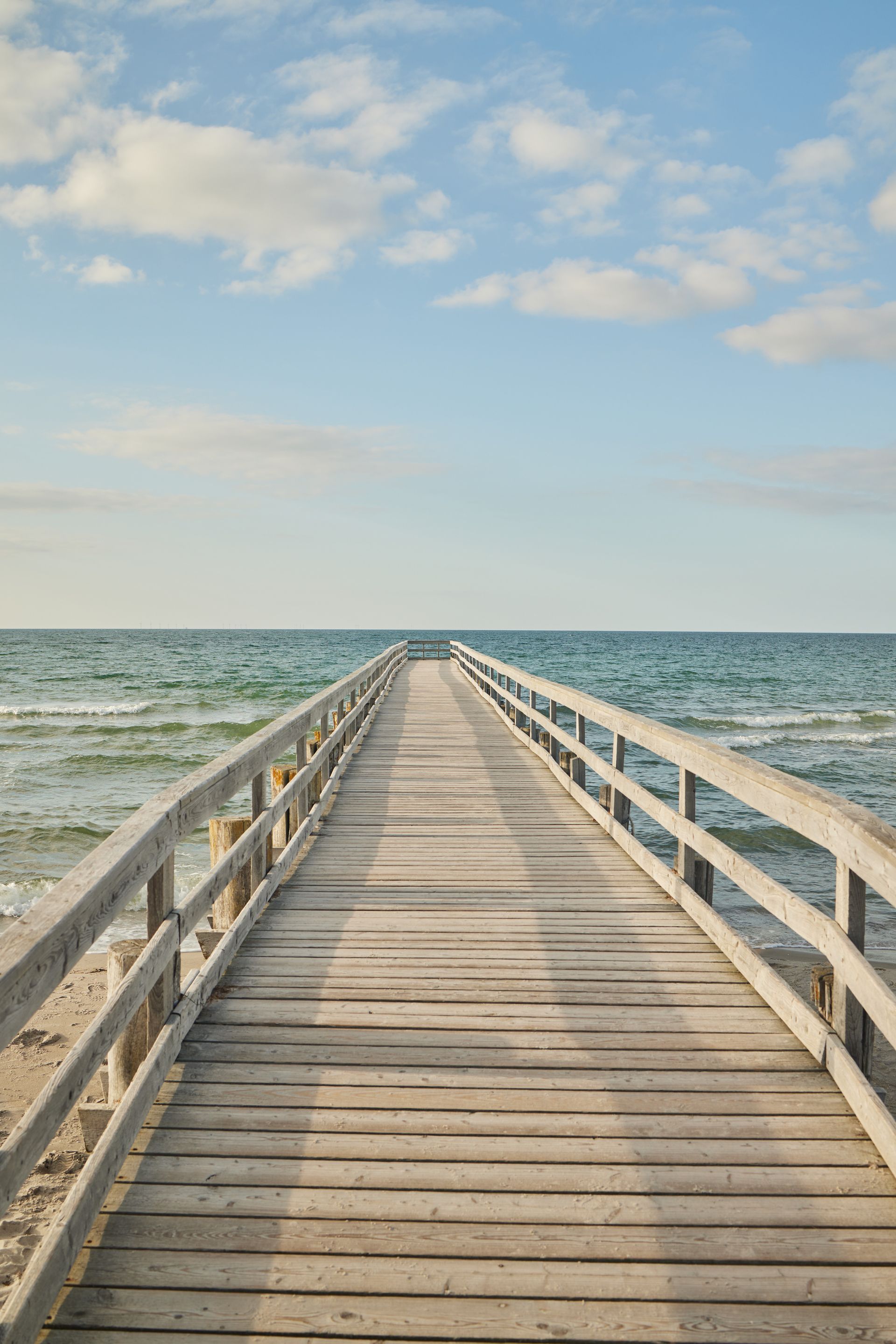 Ein Holzsteg, der in die Ostsee hineinragt, unter einem blauen Himmel mit vereinzelten Wolken.