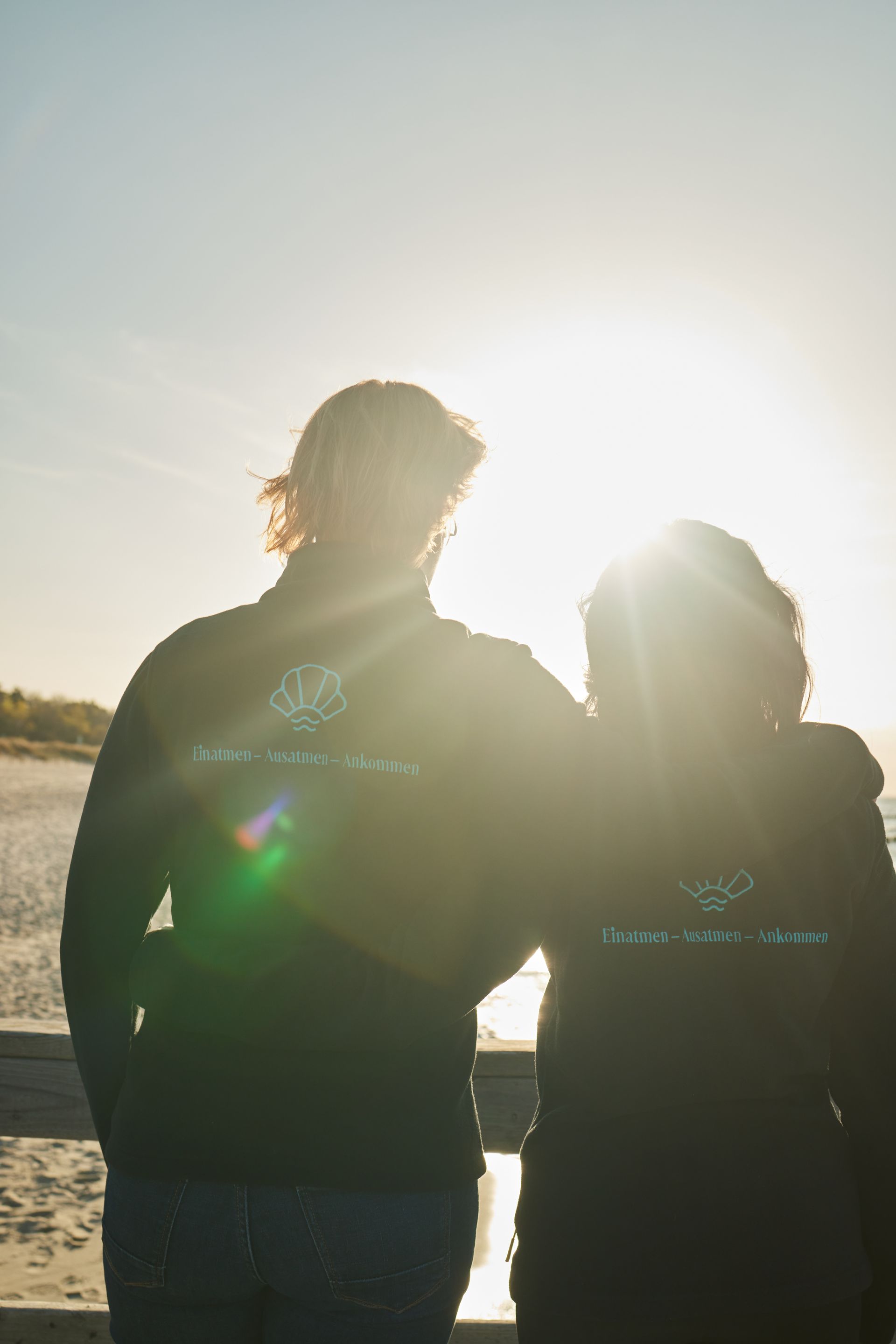 Zwei Mitarbeiter stehe auf der Seebrücke in Zingst und schauen in den Sonnenuntergang.