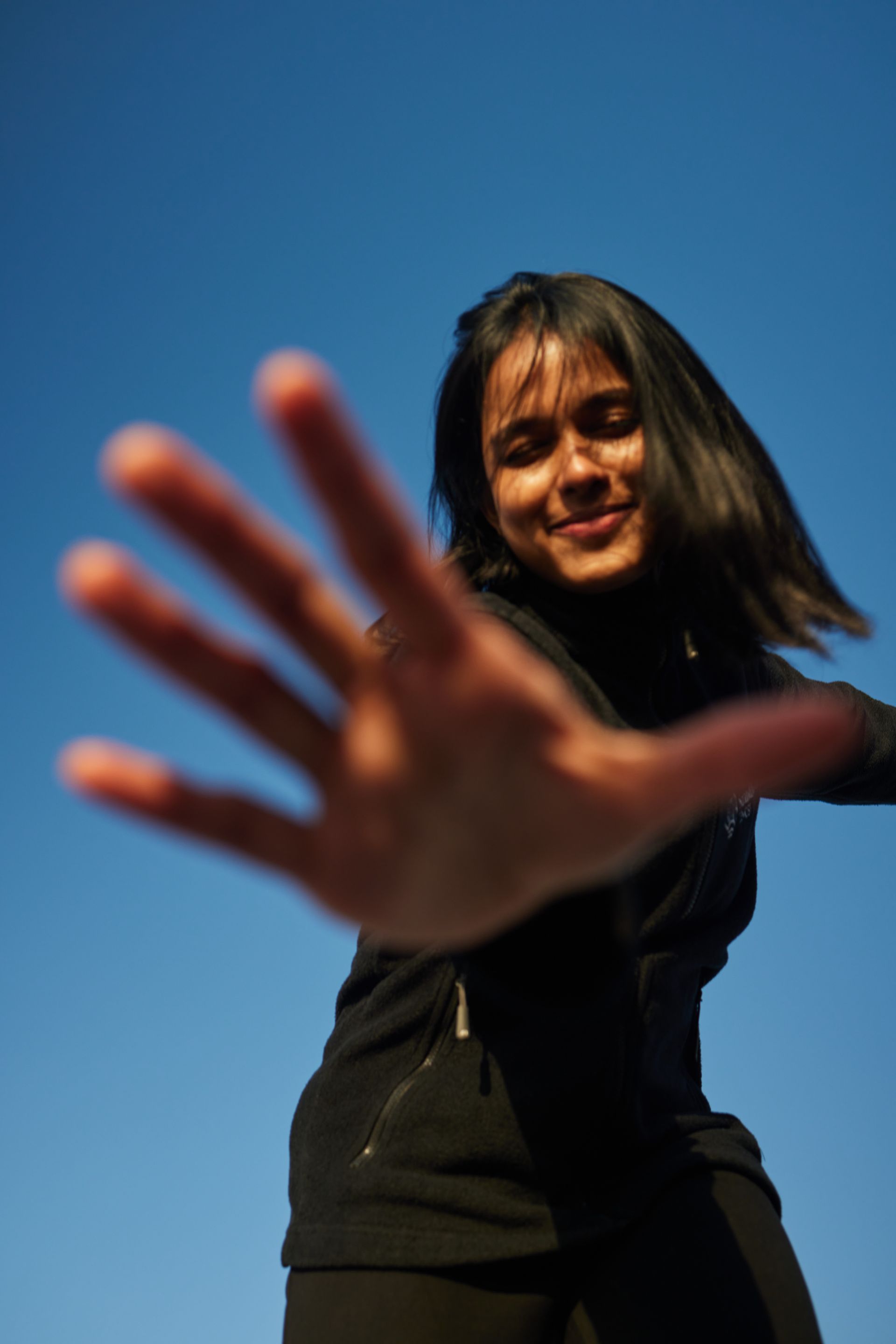 Person, die vor blauem Himmel mit offener Hand in Richtung Kamera greift.