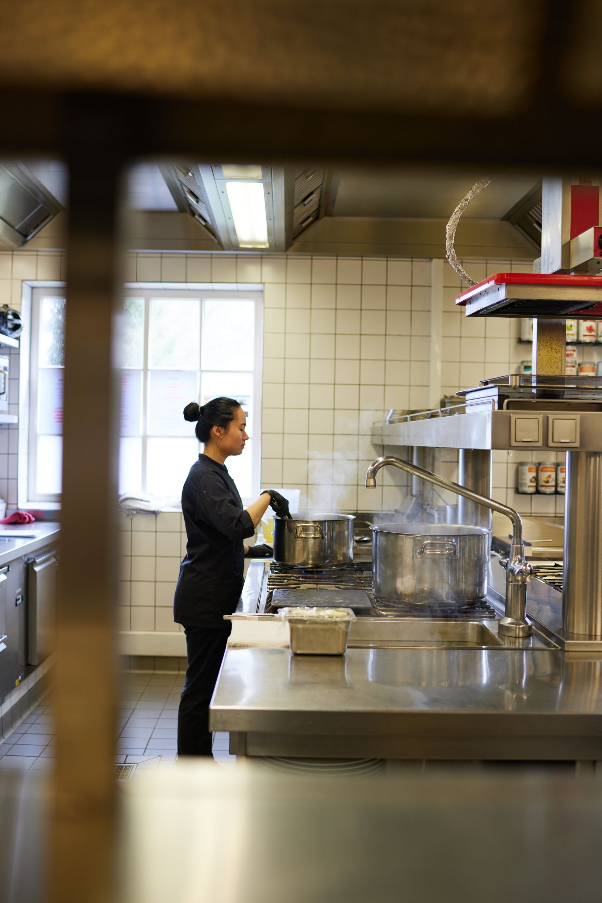 Köchin steht in der Küche vorm Herd und rührt in einem Topf.