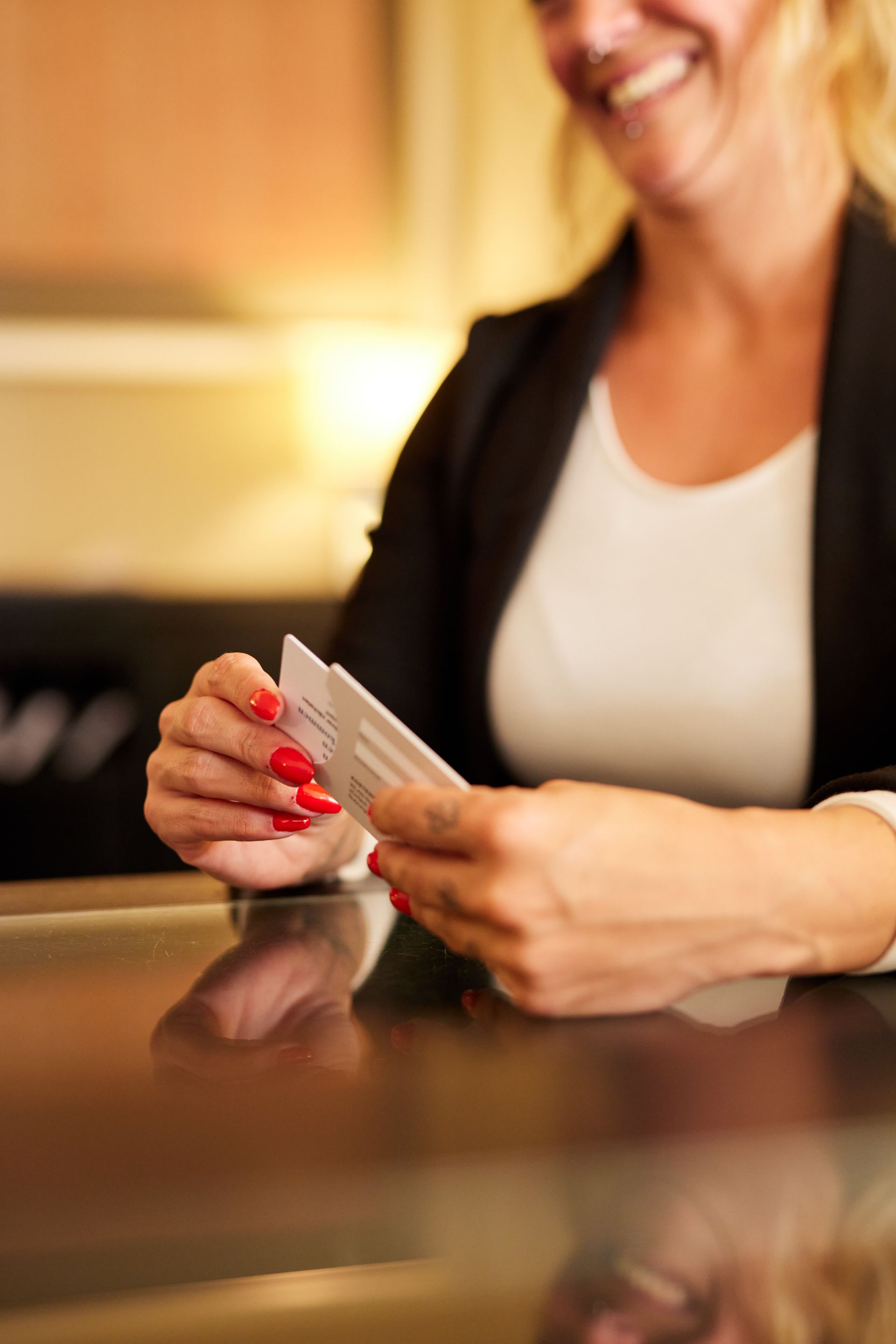 Frau im Blazer lächelt und hält Visitenkarten über eine reflektierende Oberfläche.