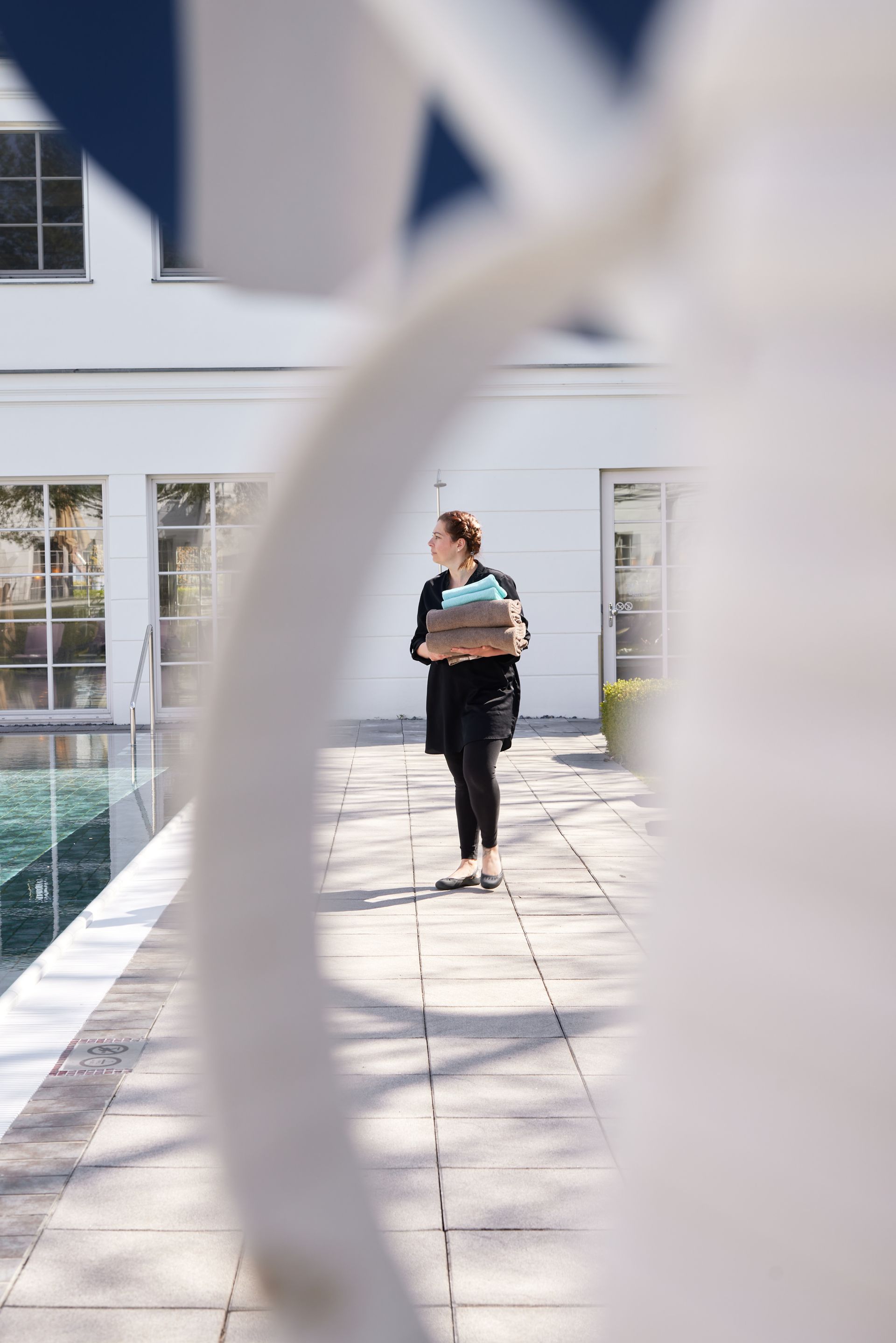 Sammle Erfahrungen für Deine Karriere Wellnessmitarbeiterin trägt Handtücher am Außenpool entlang und blickt zur Seite.