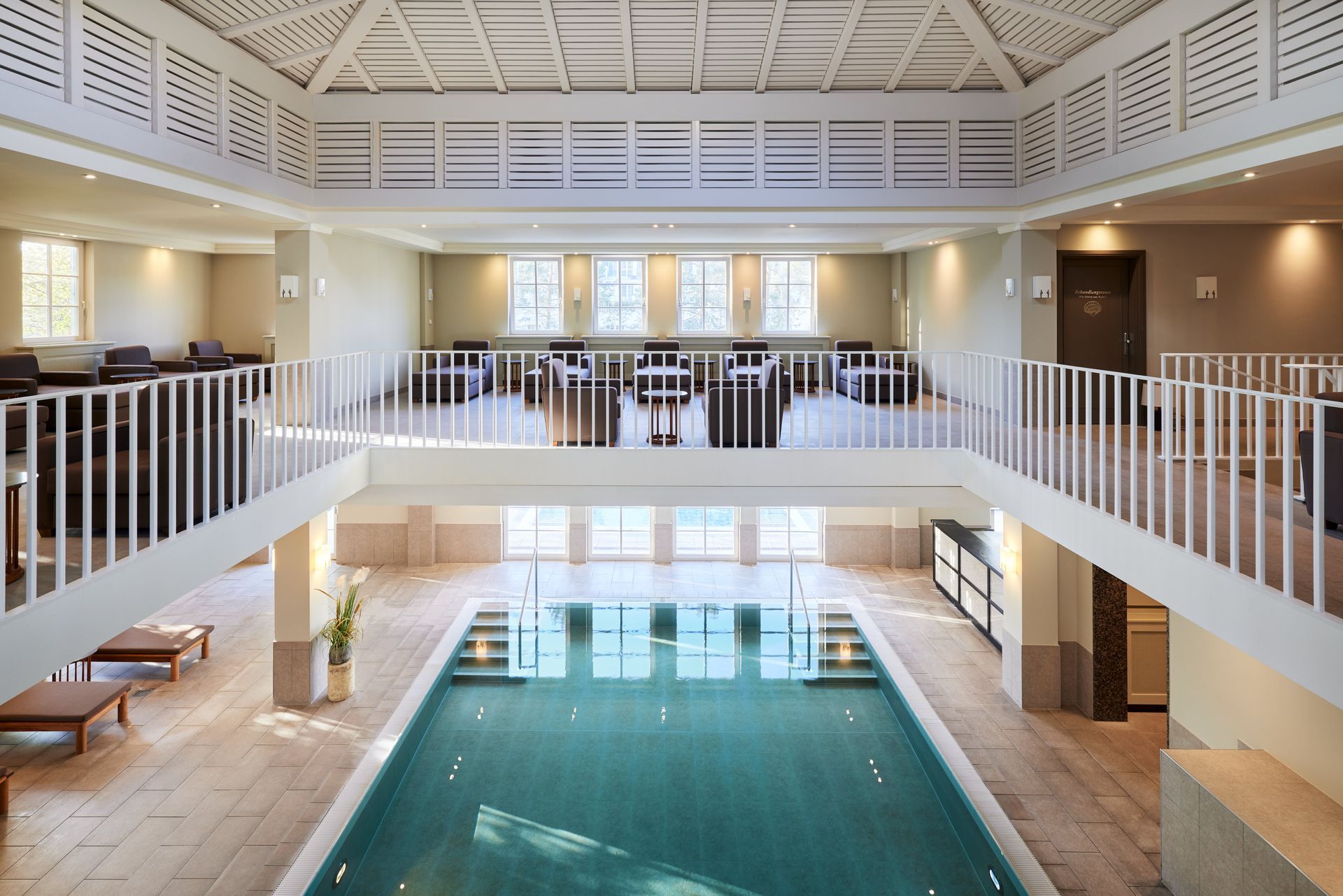 Reines Vergnügen Innenpoolbereich mit weißem Geländer, Sitzgelegenheiten im zweiten Stock und einem großen rechteckigen Pool.