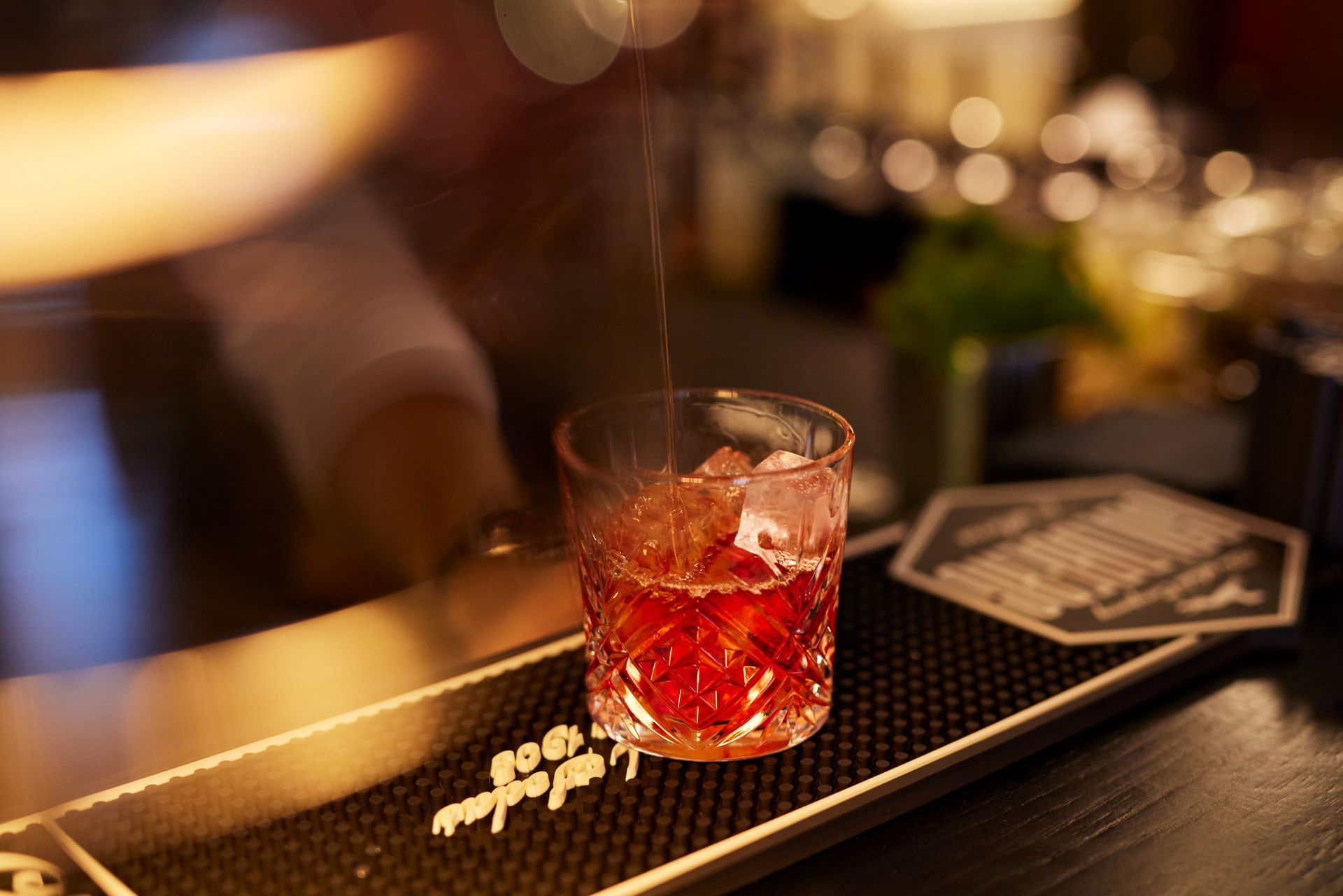 Ein Cocktail wird auf einer Bar in ein mit Eis gefülltes Tumblerglas gegossen.