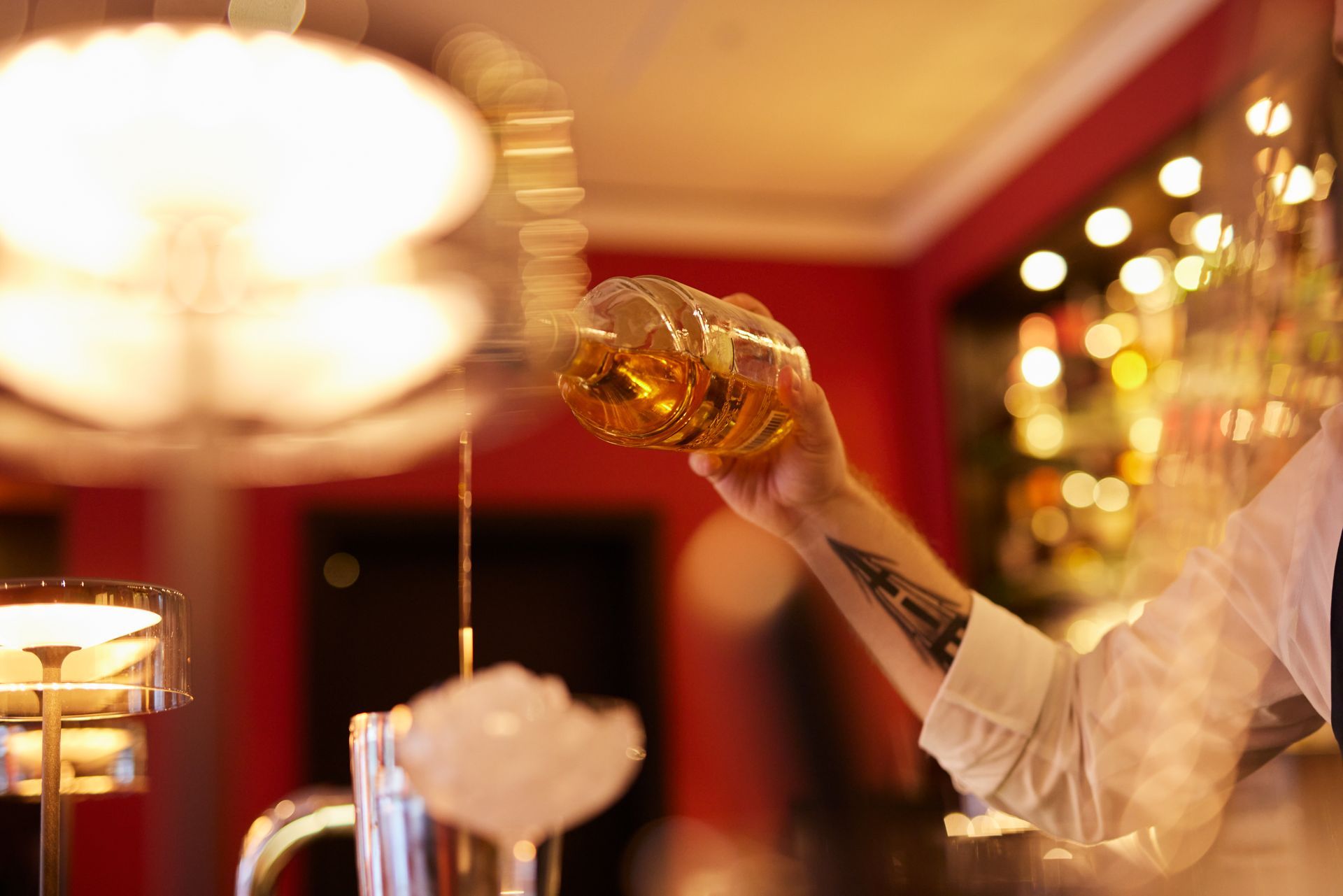 Barkeeper gießt bernsteinfarbene Flüssigkeit aus einem Glas in einen Cocktailshaker mit Eis.
