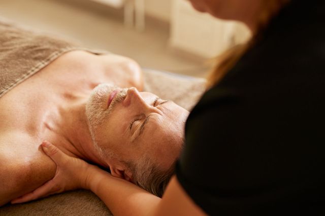 Ein Mann mit geschlossenen Augen wird von einer Person in schwarzem Hemd massiert.
