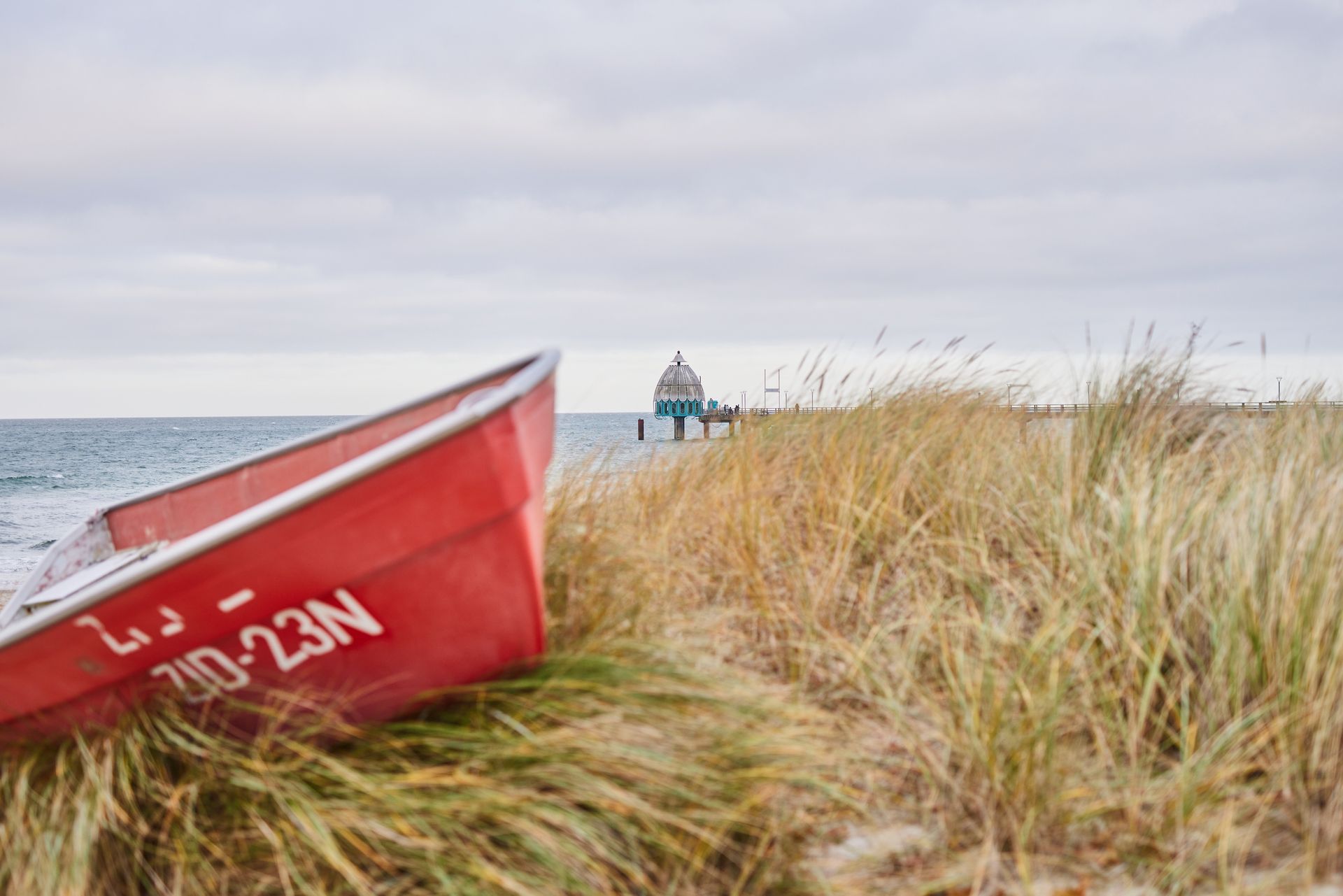 Fischerboot und Seebrücke Rotes Fischerboot zwischen dem Dünengras. Im Hintergrund ist die Seebrücke mit Ihrer Tauchgondel zusehen.