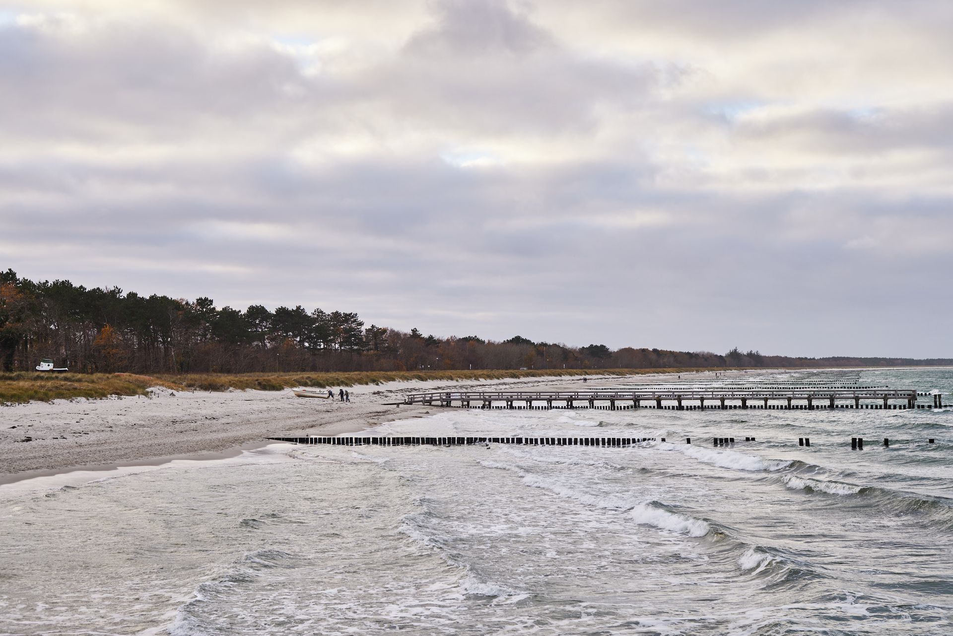 Strandszene mit bewölktem Himmel, weißem Sand und den Buhnen.