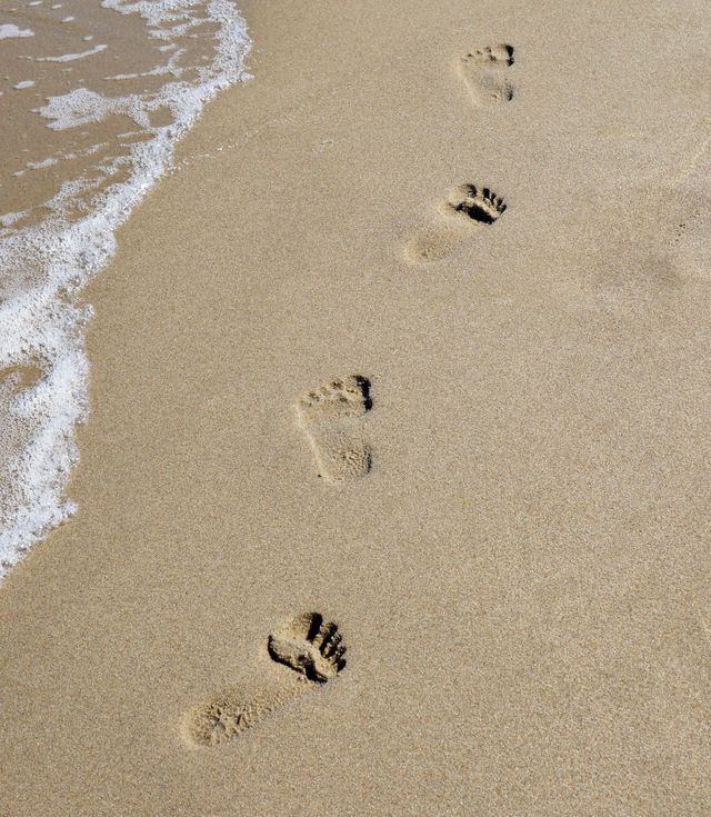 Fußabdrücke im nassen Sand nahe dem Meeresrand, teilweise von einer Welle weggespült.
