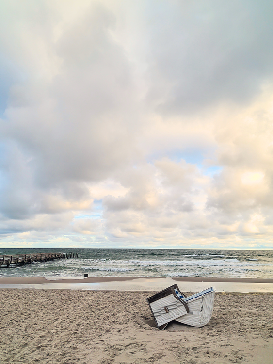 Reihen gestreifter Strandstühle an einem Sandstrand bei Sonnenuntergang, im Hintergrund die Ostsee.