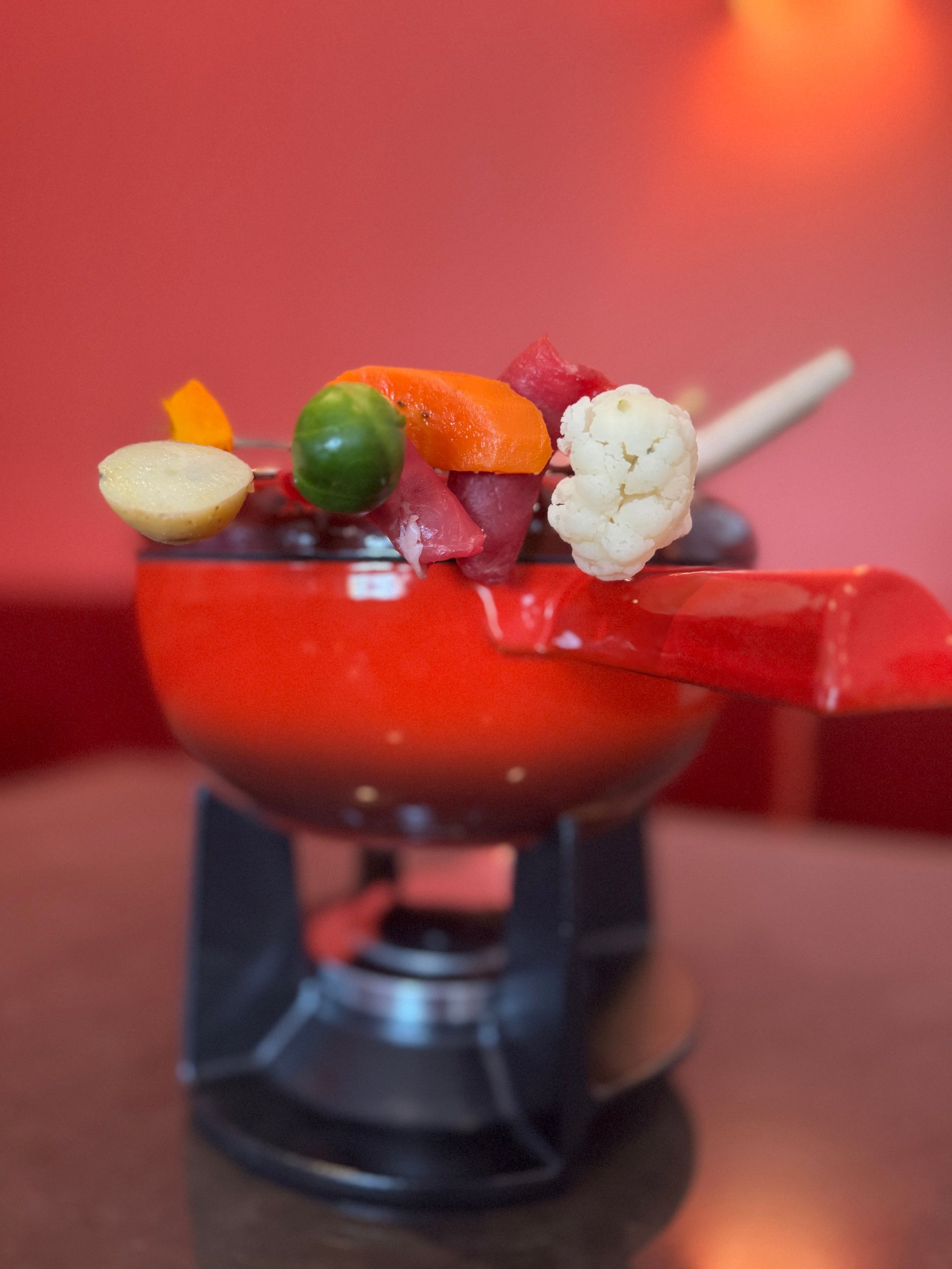 Ein Fonduetopf mit verschiedenen bunten Gemüsespießen steht auf einem Tisch.