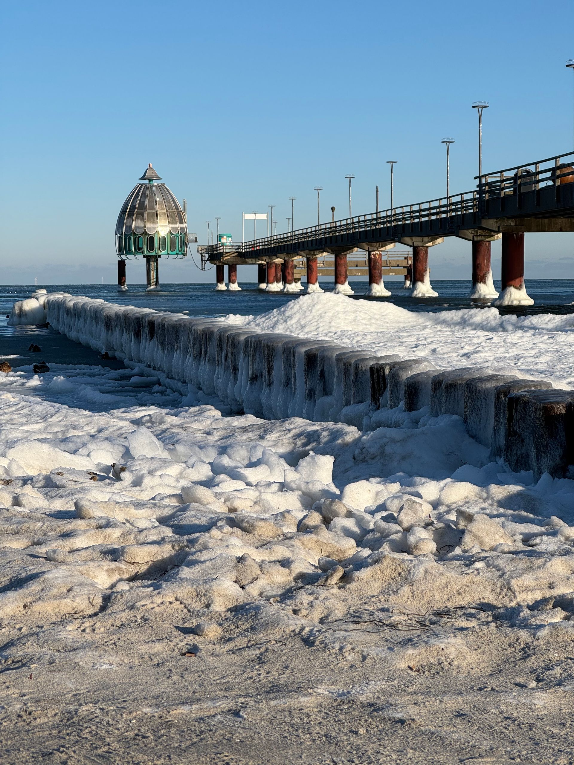 Winterzeit an der Ostsee Gefrorene Buhnen mit Eis überzogen. Im Hintergrund die Seebrücke. Blauer Himmel.