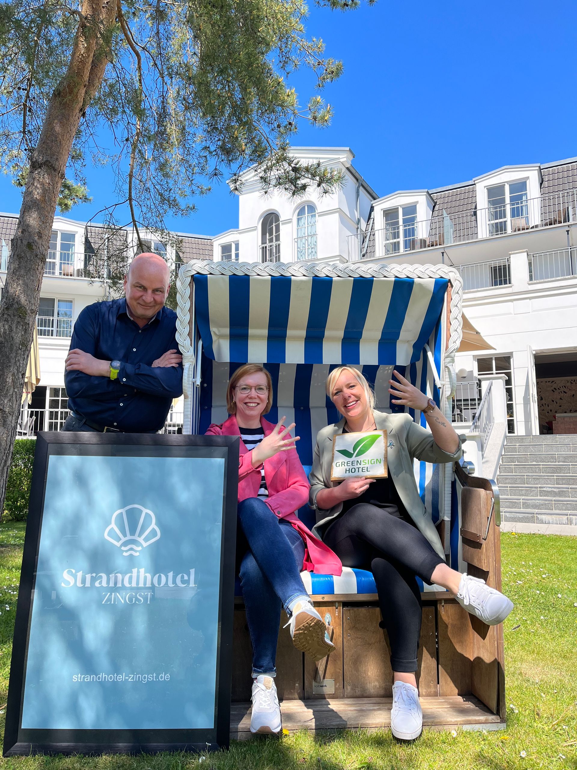 Drei Personen in einem Strandkorb. Eine Person hält das GreenSign Schild in der Hand. 