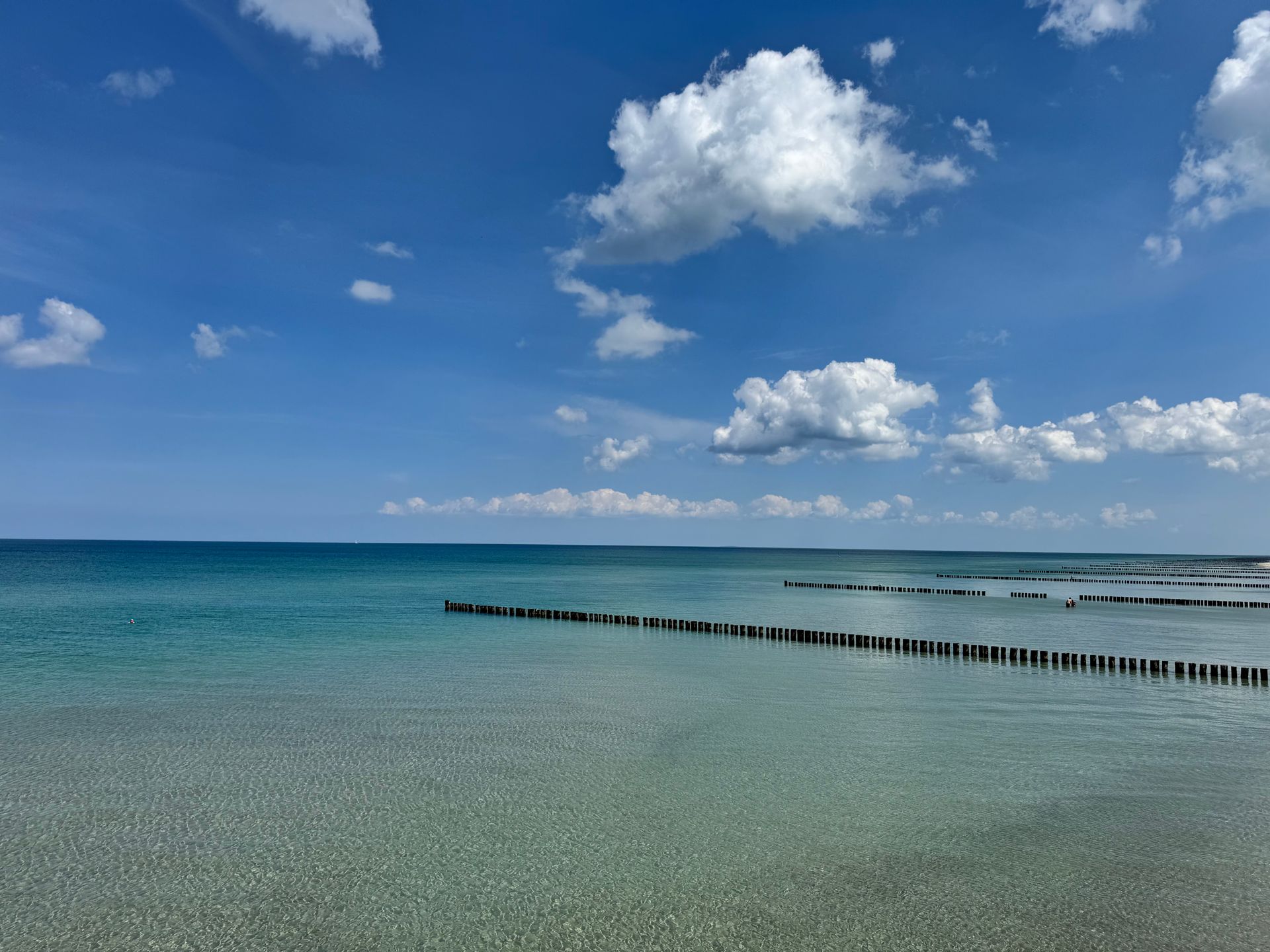 Naturklänge wirken nachweislich beruhigend auf das Gehirn Sonniger Strand mit türkisfarbener Ostsee, kleinen Wellen und einer fernen Küstenlinie unter blauem Himmel