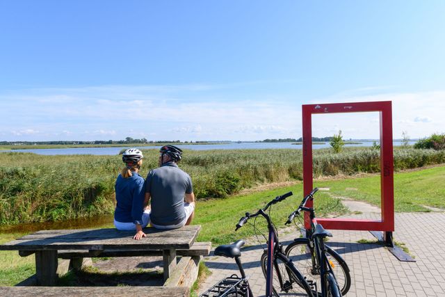 Küstenblick: Strand, erodierte Klippe, verwitterte Betonbauten, ruhiges blaues Meer, sonniger Himmel.