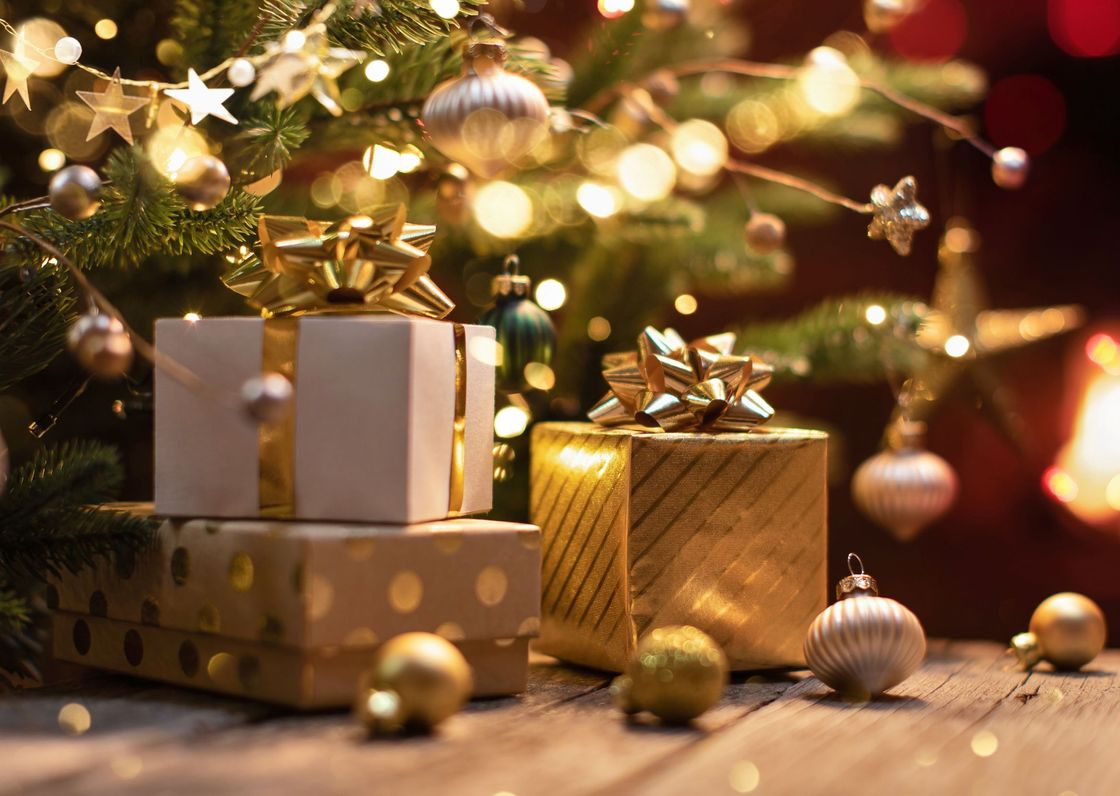 Ein Geschenk, verpackt in braunes Papier und mit grünem Band, unter einem schneebedeckten, beleuchteten Weihnachtsbaum.