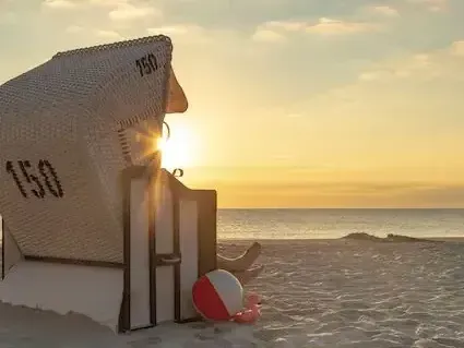 Strandstuhl am Sandstrand bei Sonnenuntergang, mit einem Strandball.