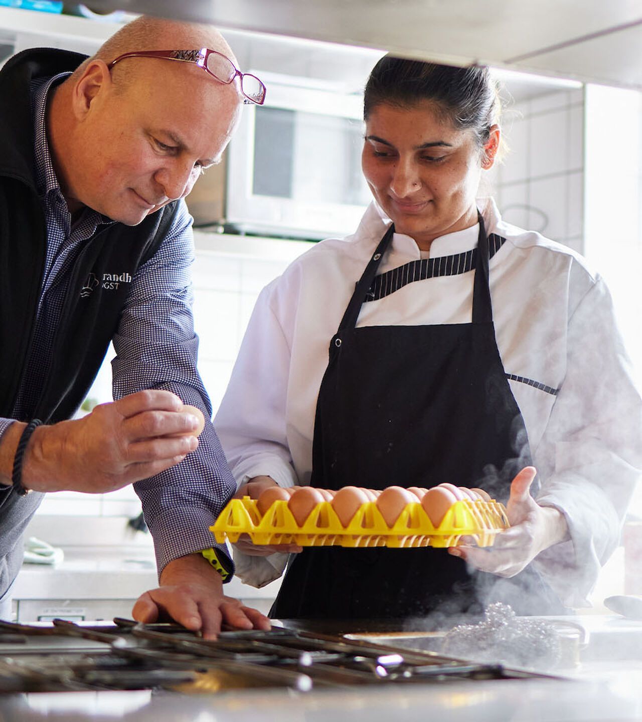 Duales Studium Ostsee Meer Strand Koch und Kollege untersuchen Eier in einer Küche. Der Koch hält ein Ei, die andere Person hält einen Eierkarton.