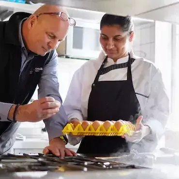 Ausbildung Mann und Frau inspizieren in einer Küche einen Eierkarton. Die Frau trägt eine Kochuniform.