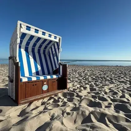 Strandstuhl mit blau-weißen Streifen an einem Sandstrand unter klarem, blauem Himmel.