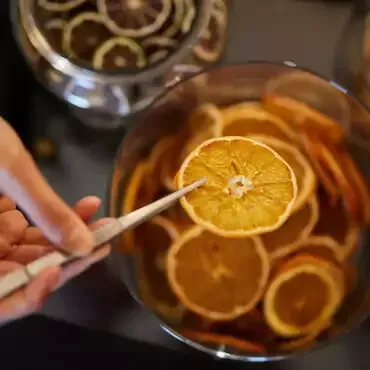 Bild von oben über eine Glas mit getrockneten Orangenscheiben, eine Scheibe wird mit einem Stäbchen aus dem Glas geholt.