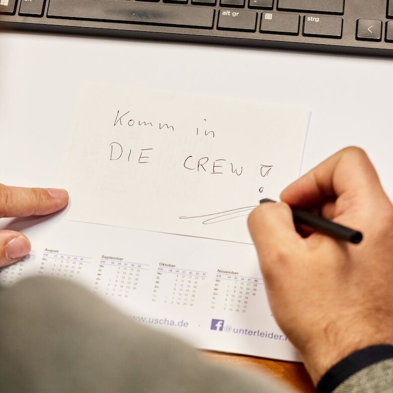 Komm in die CREW Person, die auf einen Zettel „Komm in DIE CREW!“ schreibt: