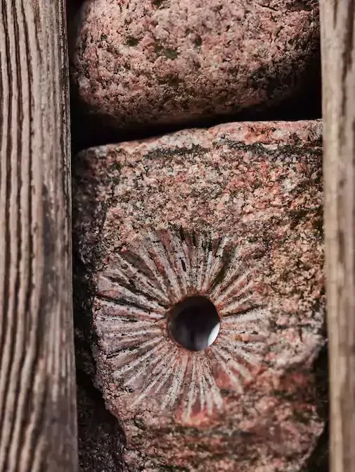 Kunst auf der Seebrücke Stein mit kreisförmigem Schnitzmuster, eingerahmt von Holzbalken und anderen Steinen.
