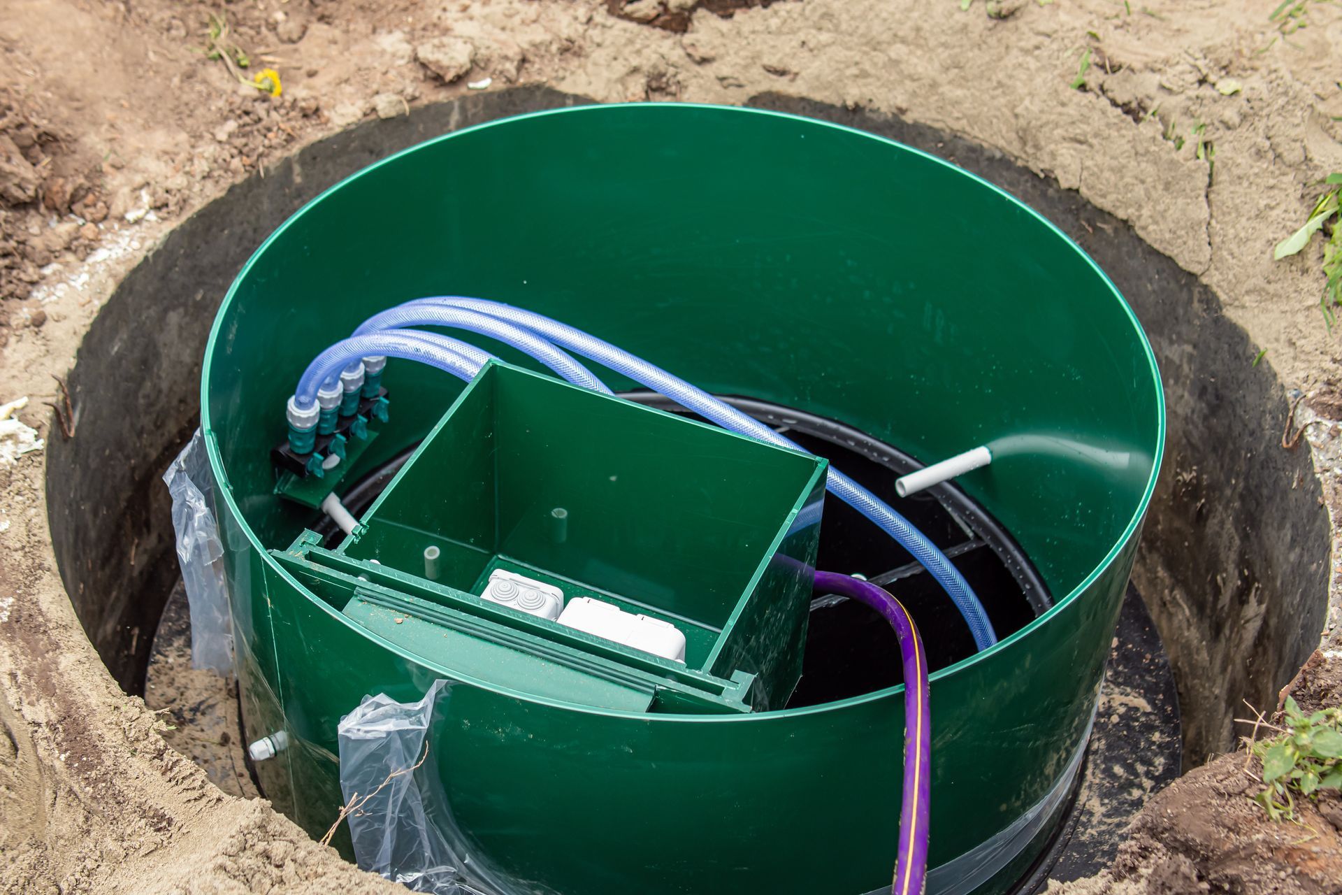 Boîtier électrique vert dans une fosse à terre avec câbles et fils apparents.