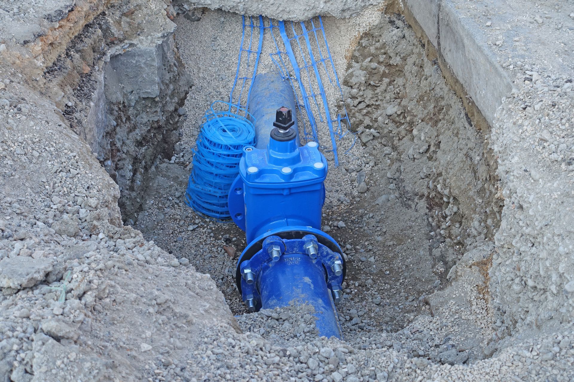 Vanne d'eau bleue dans une tranchée de terre avec un tuyau bleu raccordé.