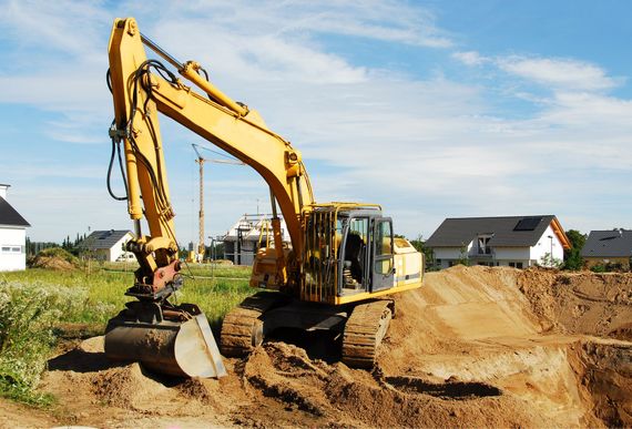 Une pelleteuse jaune creuse la terre sur un chantier de construction avec des maisons en arrière-plan.