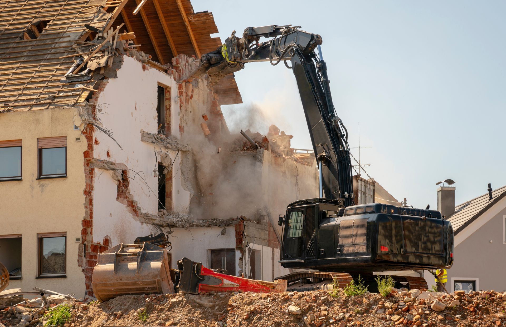 Une pelleteuse démolit une maison endommagée, soulevant poussière et débris.