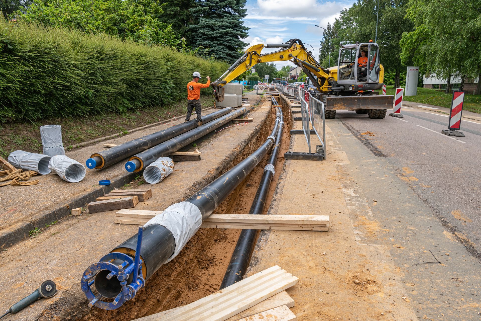 Travaux de construction routière : des ouvriers installent de gros tuyaux à côté d’une rue excavée.