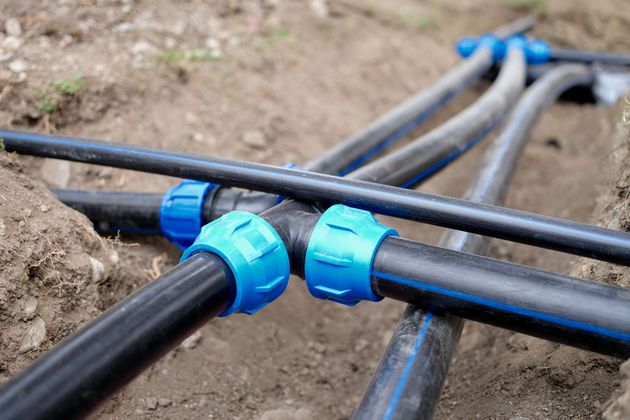 Des tuyaux d'irrigation noirs, reliés par des raccords en plastique bleu, sont installés dans une tranchée.