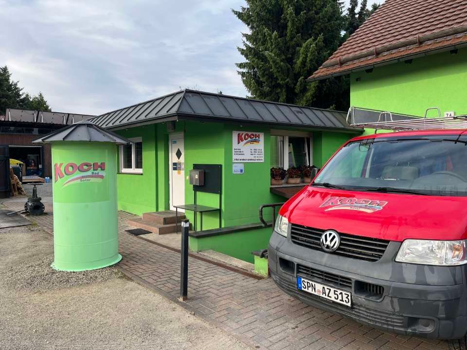 Grünes Gebäude und Silo mit einem davor geparkten roten VW-Transporter.