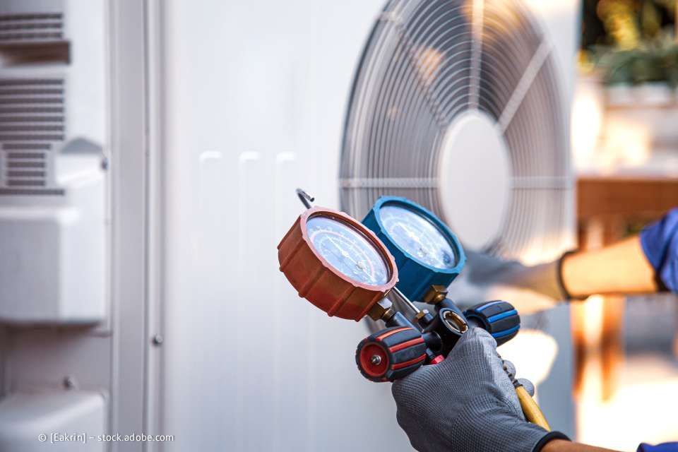 Eine Person mit grauen Handschuhen bedient Messgeräte an einer Außenklimaanlage.
