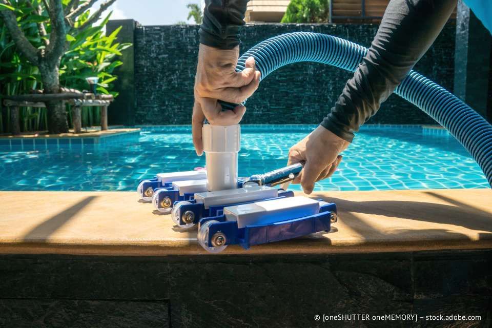 Person, die in einem Pool einen blau-weißen Poolroboter benutzt.