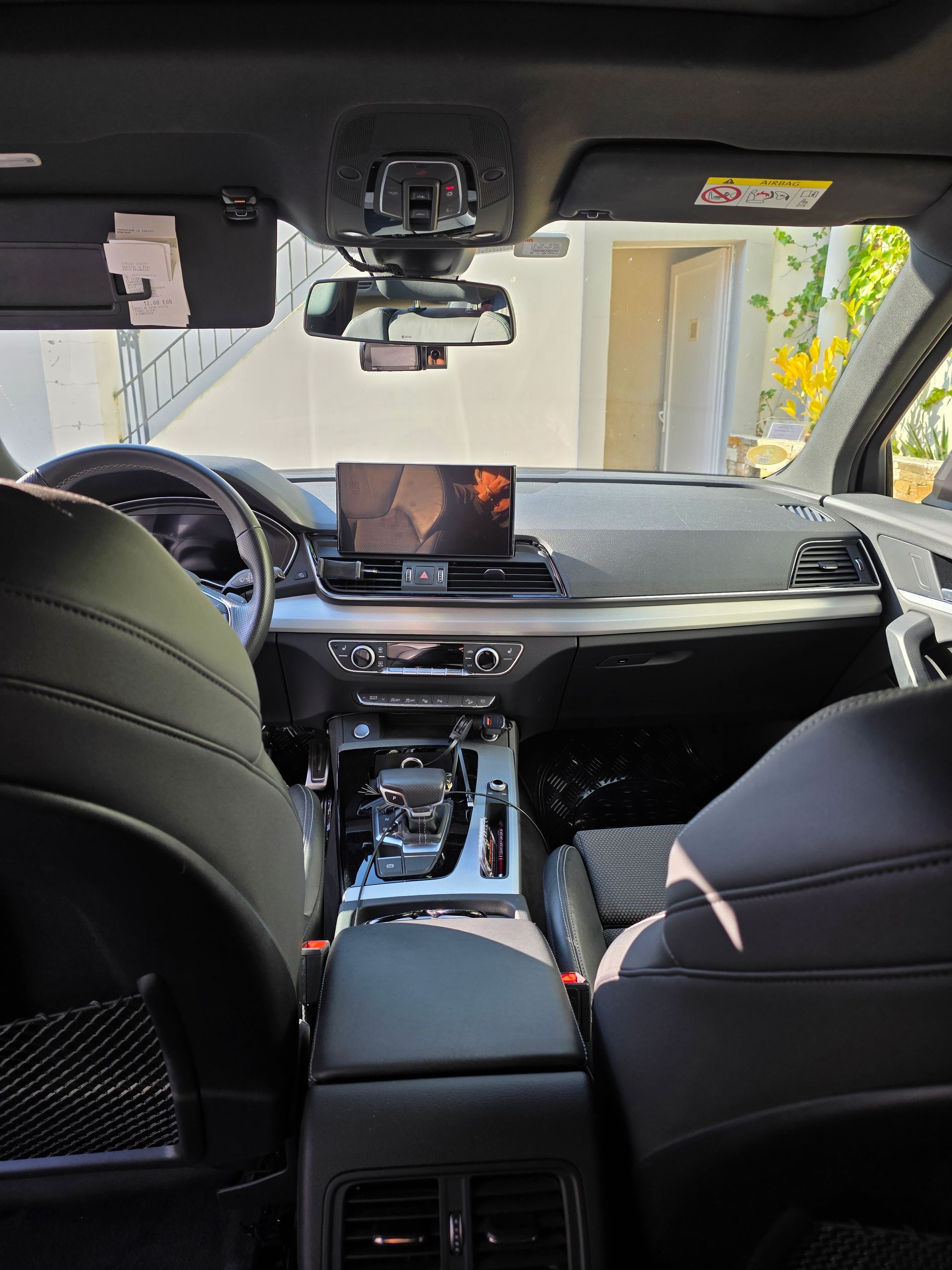 Vue intérieure depuis la banquette arrière d'une voiture moderne, montrant des sièges en cuir noir et un tableau de bord avec un écran central.