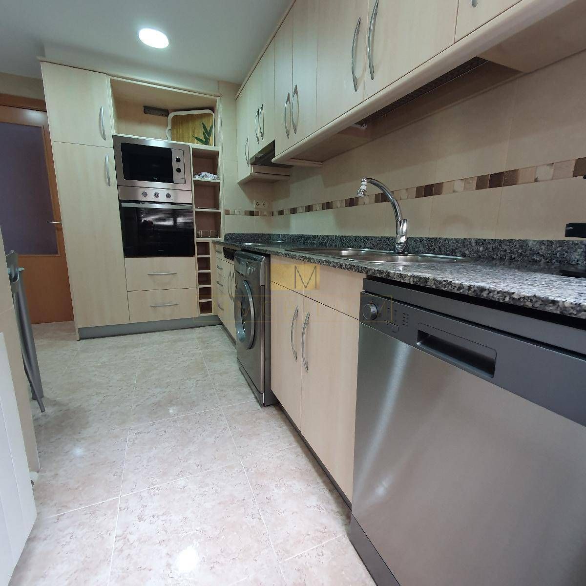 Una cocina con gabinetes de madera clara, electrodomésticos de acero inoxidable y encimera de granito.