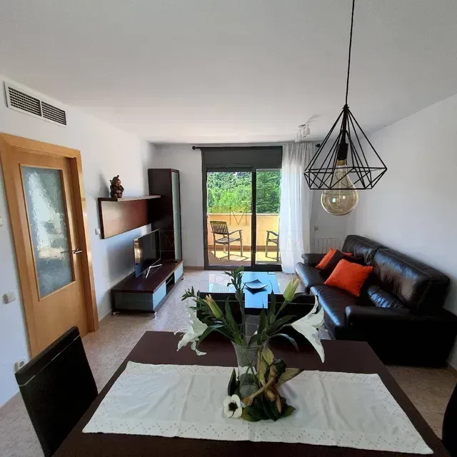 Sala de estar con sofá de cuero marrón, mesa de comedor y acceso al balcón.