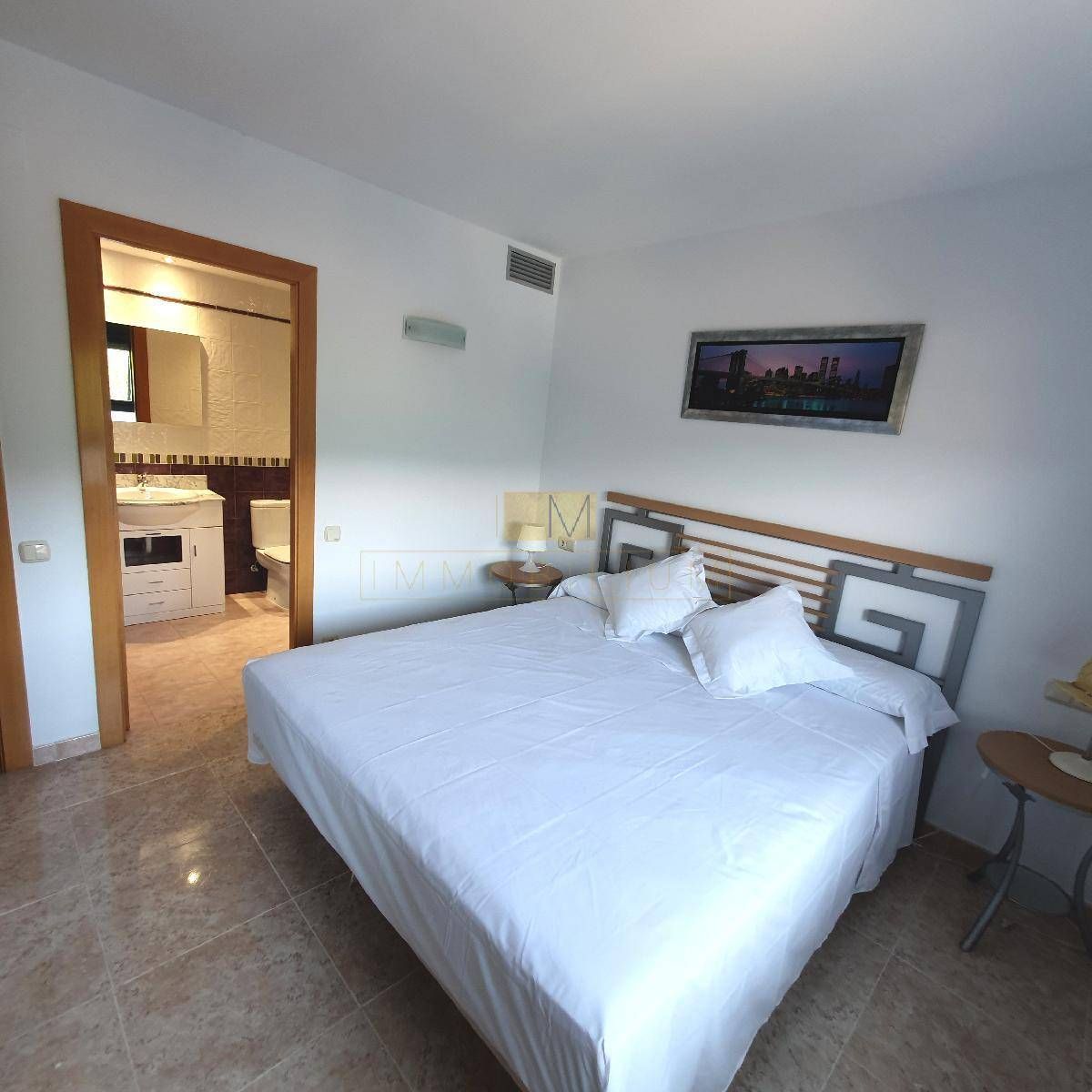 Dormitorio con cama de matrimonio, ropa de cama blanca y baño contiguo.