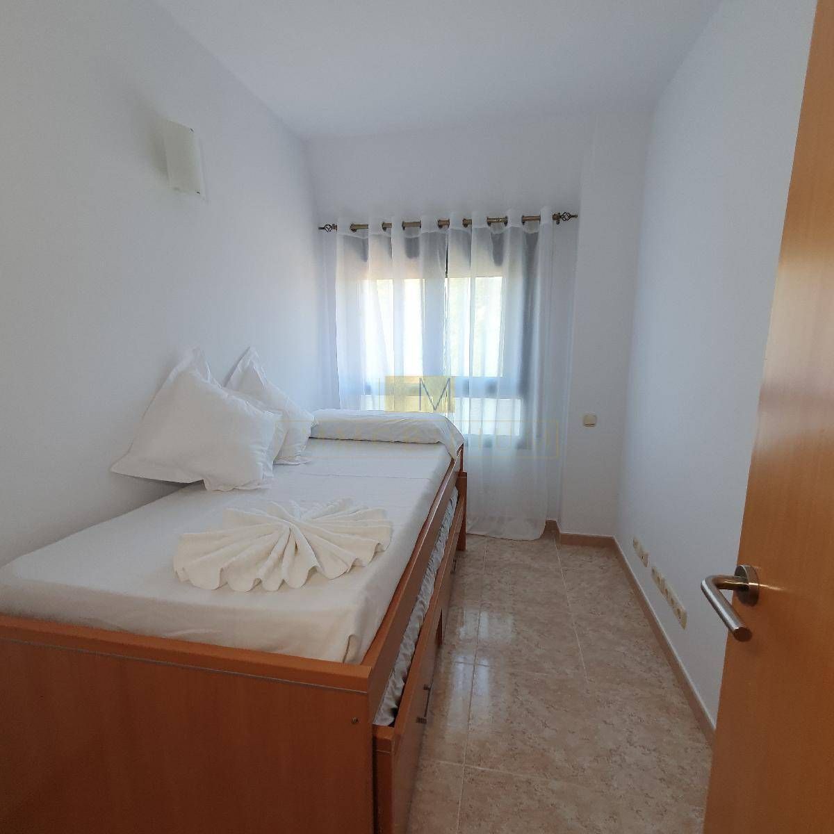 Dormitorio con cama individual, ropa de cama blanca, ventana con cortinas y molduras de madera.