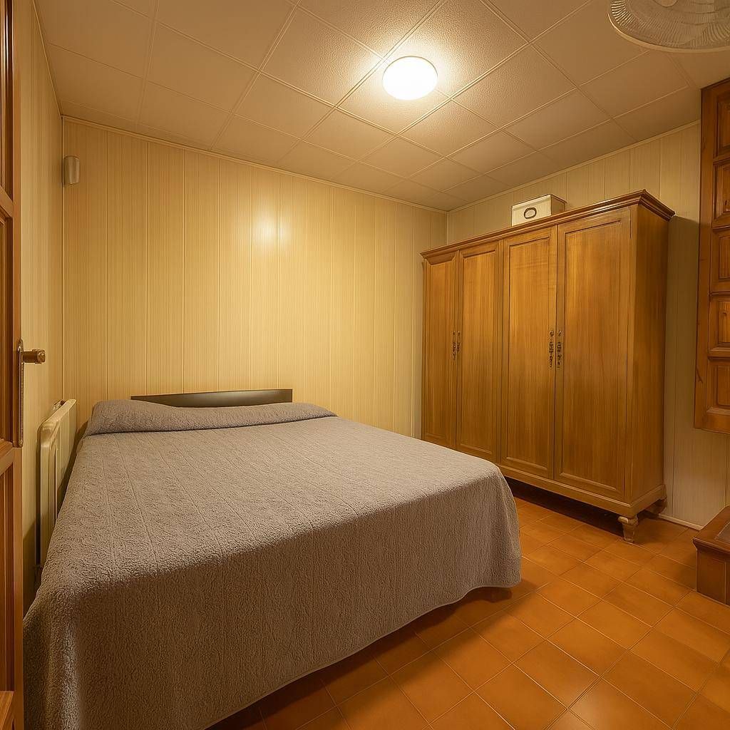 Dormitorio con cama, armario de madera y paredes revestidas de madera; iluminación cálida.